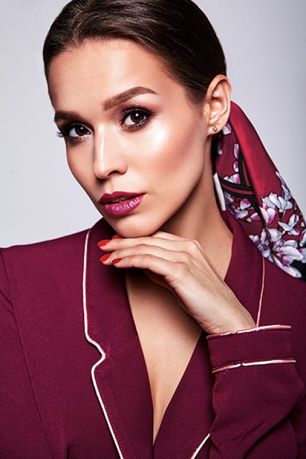 Portrait of beautiful sexy brunette woman business  model in red suit clothes with evening makeup isolated on gray background